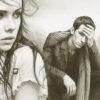 Black and white artistic image of a young woman and man with melancholic expressions; the woman looks away thoughtfully while the man sits in a field, leaning forward with his hand on his forehead, appearing distressed.